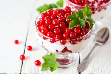 Yoğurt tatlı kırmızı kuş üzümü ile ve Beyaz ahşap zemin üzerinde yapraklarla süslenmiş