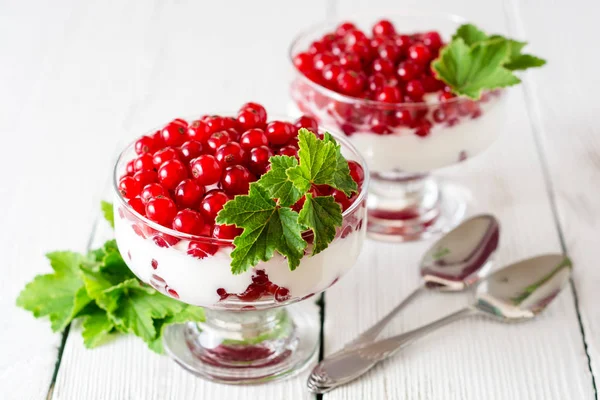 Yoğurt tatlı kırmızı kuş üzümü ile ve Beyaz ahşap zemin üzerinde yapraklarla süslenmiş