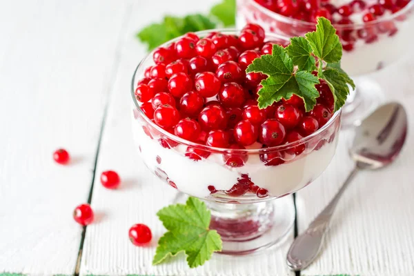 Yoğurt tatlı kırmızı kuş üzümü ile ve Beyaz ahşap zemin üzerinde yapraklarla süslenmiş