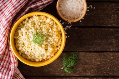 Koyu ahşap zemin üzerine sarı seramik kase dereotu ile Bulgur