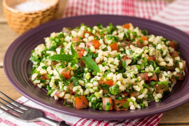 Bulgur, domates, maydanoz, yeşil soğan ve nane plaka üzerinde ahşap masa Tabbouleh salatası.