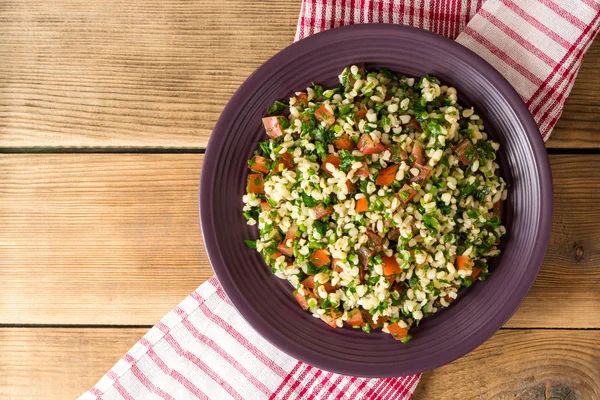 Salade de taboulé au bulgur, tomates, persil, oignon vert et menthe dans une assiette sur une table en bois . — Photo