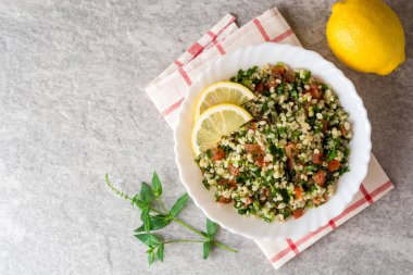 Bulgur, domates, maydanoz, yeşil soğan ve nane plaka gri taş masada Tabbouleh salatası.
