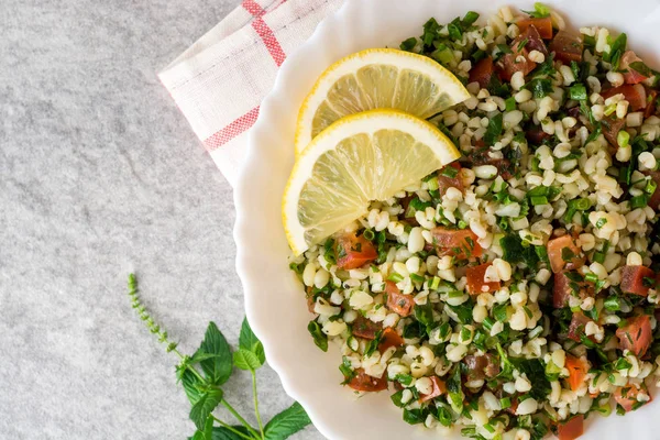 Bulgur, domates, maydanoz, yeşil soğan ve nane plaka gri taş masada Tabbouleh salatası.