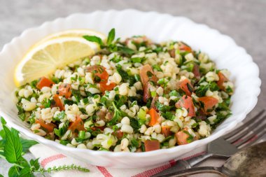Bulgur, domates, maydanoz, yeşil soğan ve nane plaka gri taş masada Tabbouleh salatası.