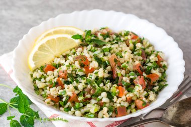 Bulgur, domates, maydanoz, yeşil soğan ve nane plaka gri taş masada Tabbouleh salatası.