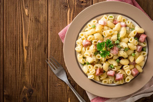 Těstoviny s hráškem, cibulí, slaninou a sýrem na dřevěné pozadí — Stock fotografie