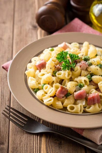 Yeşil bezelye, soğan, pastırma ve ahşap zemin üzerine peynir ile makarna