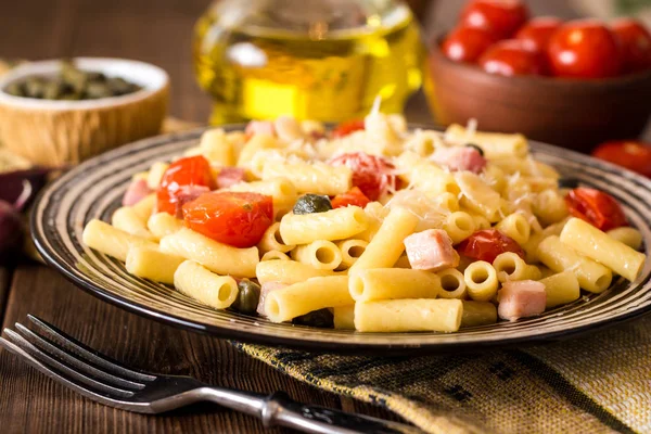 Pasta con tocino, ajo, tomates, alcaparras y queso parmesano en plato sobre fondo de madera oscura . — Foto de Stock