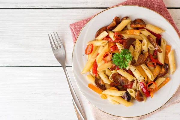 Penne pasta con champiñones, pimiento, chile y perejil en plato blanco sobre fondo de madera blanca . — Foto de Stock