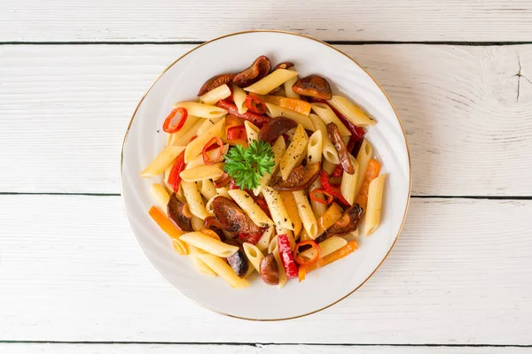 Mantar, biber, biber ve maydanoz Beyaz ahşap zemin üzerinde beyaz tabakta Penne makarna.