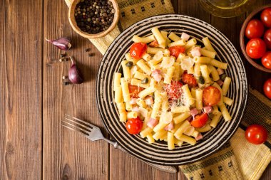 Plaka koyu ahşap arka plan üzerinde pastırma, sarımsak, domates, Kapari ve parmesan peynirli makarna.