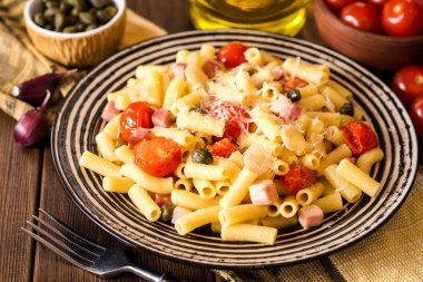 Plaka koyu ahşap arka plan üzerinde pastırma, sarımsak, domates, Kapari ve parmesan peynirli makarna.