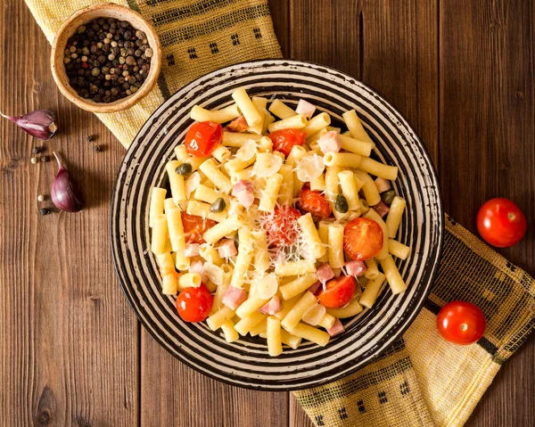 Plaka koyu ahşap arka plan üzerinde pastırma, sarımsak, domates, Kapari ve parmesan peynirli makarna.