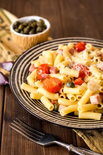 Plaka koyu ahşap arka plan üzerinde pastırma, sarımsak, domates, Kapari ve parmesan peynirli makarna.