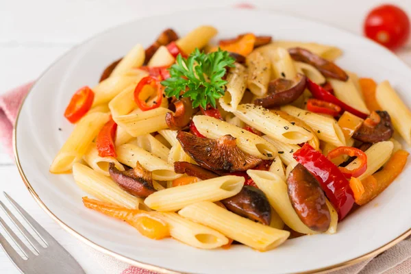 Penne pasta con champiñones, pimiento, chile y perejil en plato blanco sobre fondo de madera blanca . — Foto de Stock