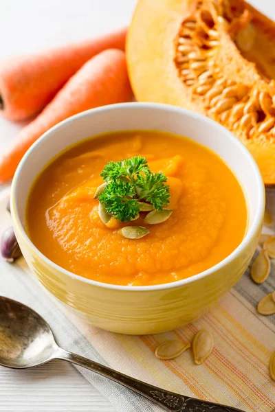 Soupe à la crème de citrouille et carotte avec graines de citrouille et persil dans un bol sur fond de bois blanc . — Photo