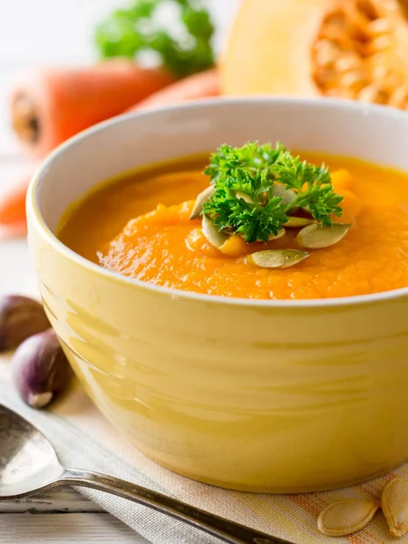 Soupe à la crème de citrouille et carotte avec graines de citrouille et persil dans un bol sur fond de bois blanc . — Photo
