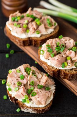 Açık sandviçler süzme peynir, konserve ton balığı ve siyah ahşap zemin üzerine yeşil soğan ile.