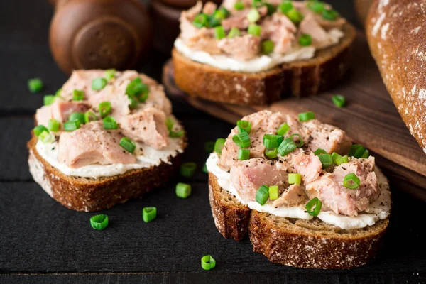 Open broodjes met kwark, tonijn in blik en groene uien op zwarte houten achtergrond. — Stockfoto