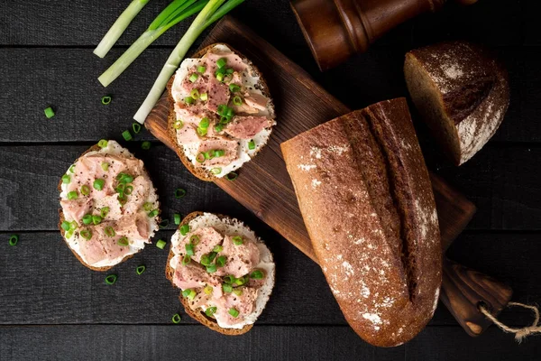 Offene Sandwiches mit Quark, Thunfischkonserven und grünen Zwiebeln auf schwarzem Holzhintergrund. — Stockfoto