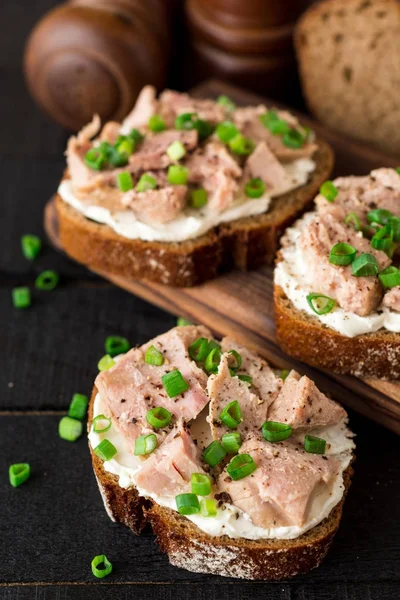 Open broodjes met kwark, tonijn in blik en groene uien op zwarte houten achtergrond. — Stockfoto