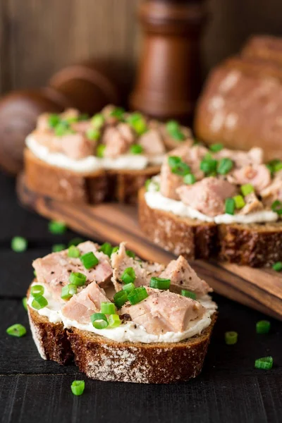 Open broodjes met kwark, tonijn in blik en groene uien op zwarte houten achtergrond. — Stockfoto