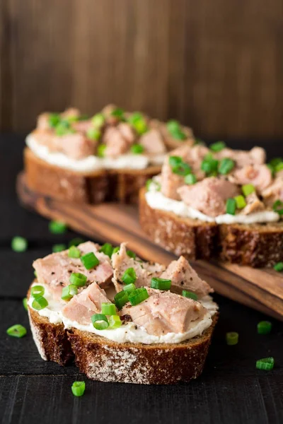 Sandwiches abiertos con requesón, atún enlatado y cebolla verde sobre fondo de madera negra . — Foto de Stock