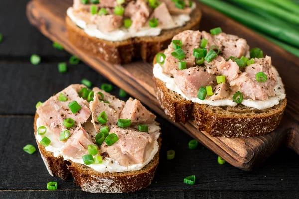 Nyitott szendvicsek, túró, konzerv tonhal és zöld hagyma, fekete fa háttér. — Stock Fotó