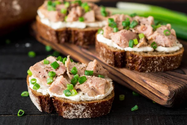 Open broodjes met kwark, tonijn in blik en groene uien op zwarte houten achtergrond. — Stockfoto