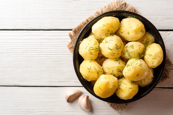 Patatas hervidas con eneldo en un tazón sobre fondo de madera blanca . —  Fotos de Stock