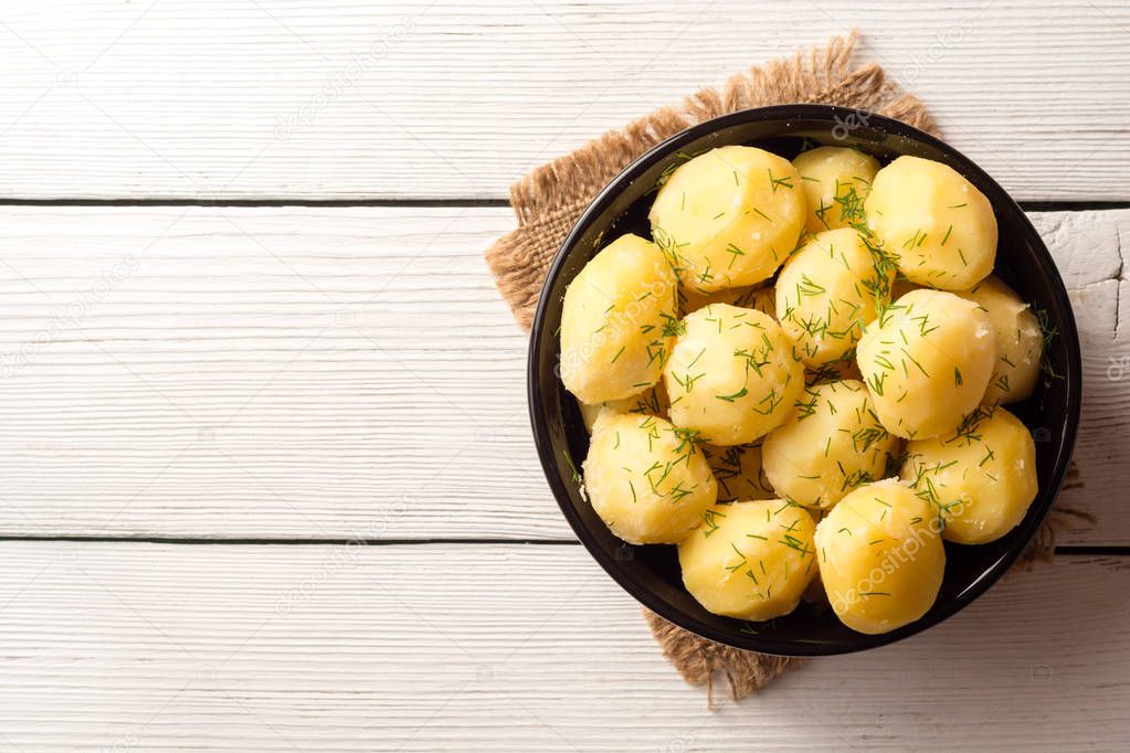 Boiled potatoes with dill in bowl on white wooden background.
