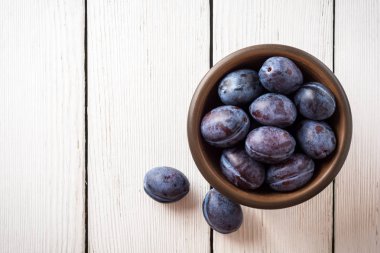 Beyaz ahşap zemin üzerinde seramik kase taze Erik.