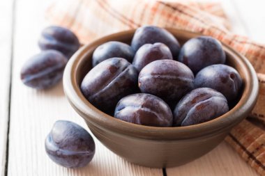 Beyaz ahşap zemin üzerinde seramik kase taze Erik.