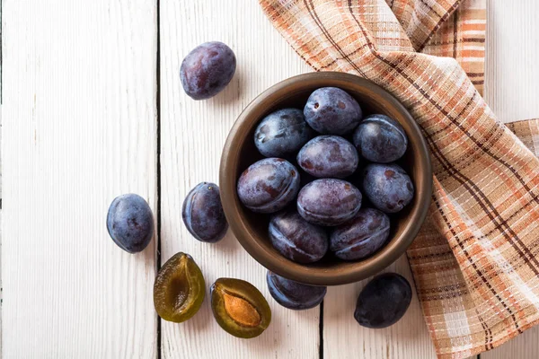 Fresh plums in ceramic bowl on white wooden background. — Stock Photo, Image