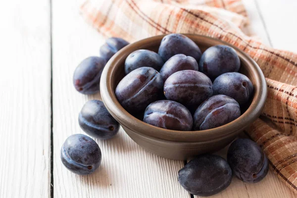 Fresh plums in ceramic bowl on white wooden background. — Stock Photo, Image