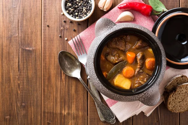 Meat stew with vegetables in ceramic pot on wooden table. — Stock Photo, Image