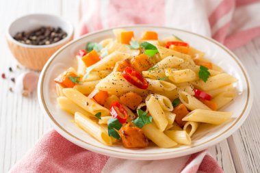 Penne makarna ile kabak, biber ve maydanoz plaka Beyaz ahşap zemin üzerinde
