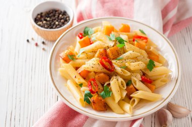 Penne makarna ile kabak, biber ve maydanoz plaka Beyaz ahşap zemin üzerinde