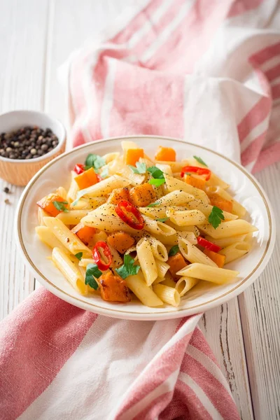 Penne pasta con calabaza, chile y perejil en plato sobre fondo de madera blanca — Foto de Stock