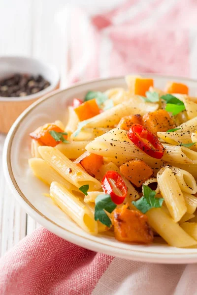 Penne pasta con calabaza, chile y perejil en plato sobre fondo de madera blanca — Foto de Stock