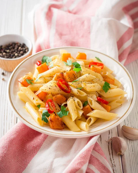 Penne pasta con calabaza, chile y perejil en plato sobre fondo de madera blanca — Foto de Stock