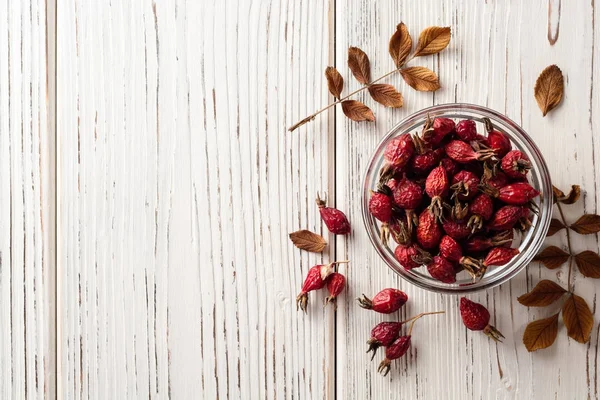 Rosa canina essiccata in ciotola di vetro su fondo di legno bianco — Foto Stock