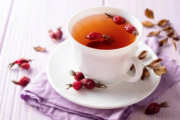 Φλιτζάνι τσάι βοτάνων από Κυνόρροδα σε μοβ φόντο ξύλινη — Φωτογραφία Αρχείου