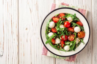 Roka, domates, mozzarella peyniri ve ceviz Beyaz ahşap zemin üzerinde taze salata.