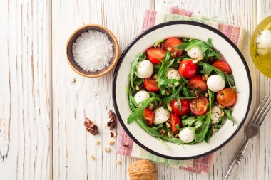 Roka, domates, mozzarella peyniri ve ceviz Beyaz ahşap zemin üzerinde taze salata.