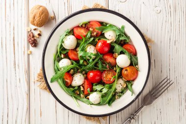 Roka, domates, mozzarella peyniri ve ceviz Beyaz ahşap zemin üzerinde taze salata.