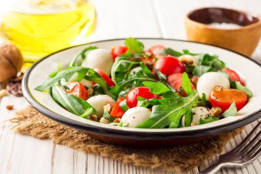 Roka, domates, mozzarella peyniri ve ceviz Beyaz ahşap zemin üzerinde taze salata.