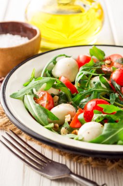 Roka, domates, mozzarella peyniri ve ceviz Beyaz ahşap zemin üzerinde taze salata.