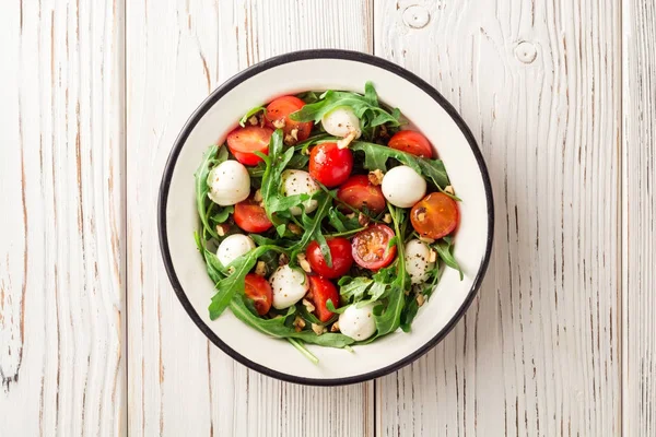 Roka, domates, mozzarella peyniri ve ceviz Beyaz ahşap zemin üzerinde taze salata.